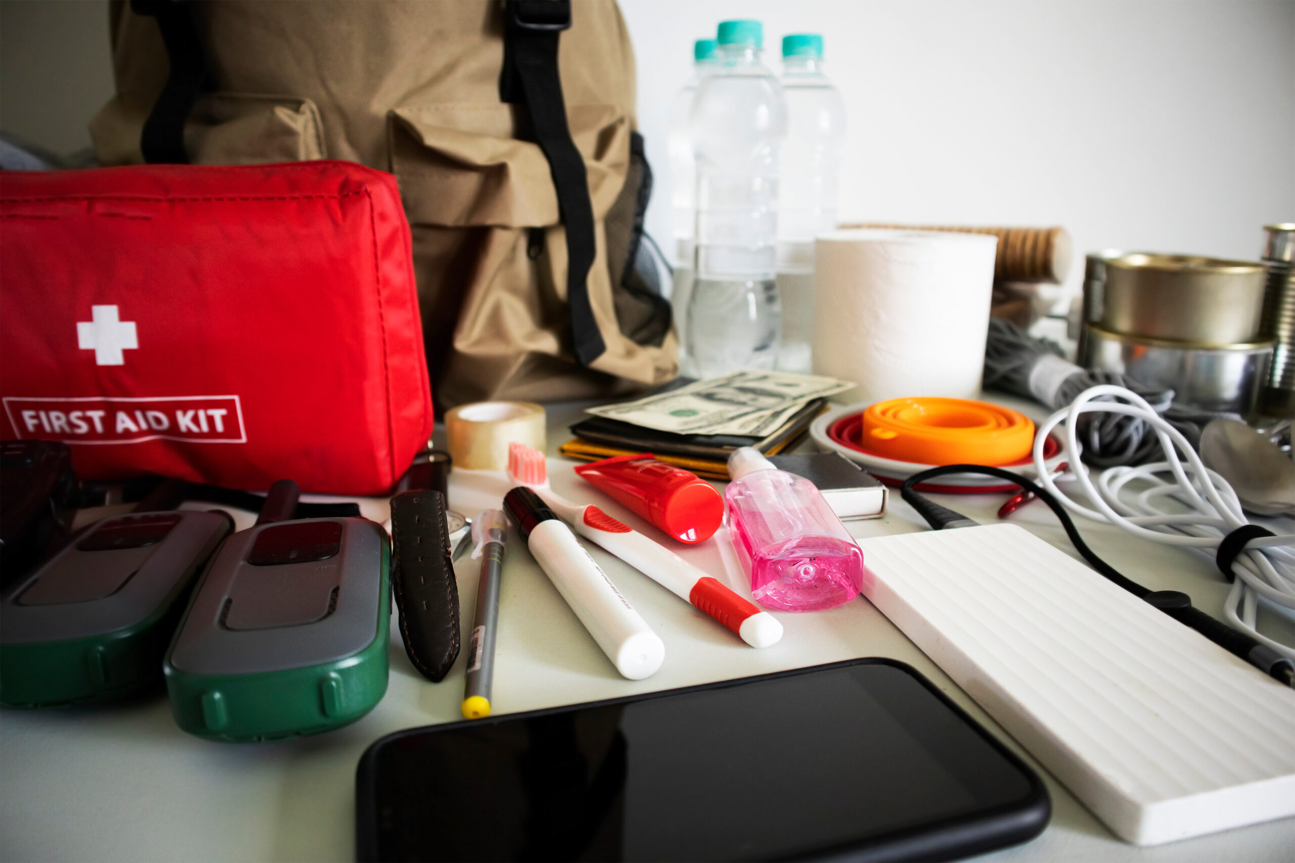 Emergency backpack equipment organized on the table. Documents, water,food, first aid kit and another items needed to survive.