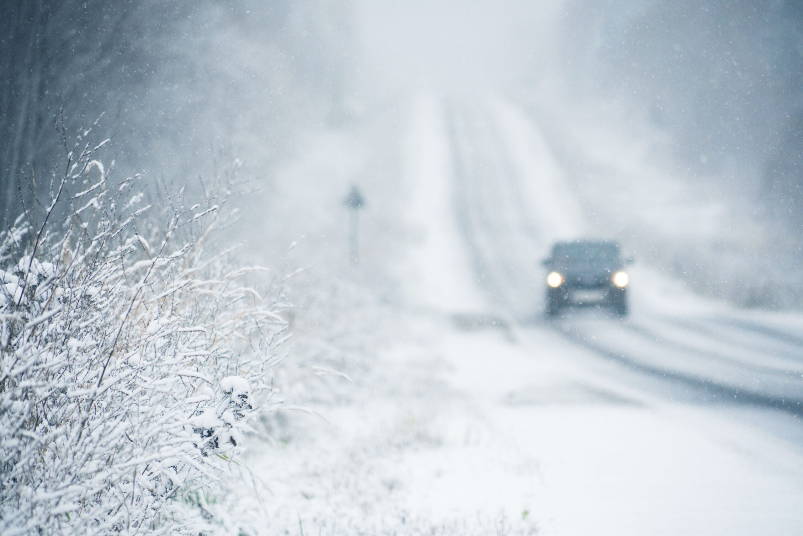 The car is driving on a winter road in a blizzard. Focus on foreground.