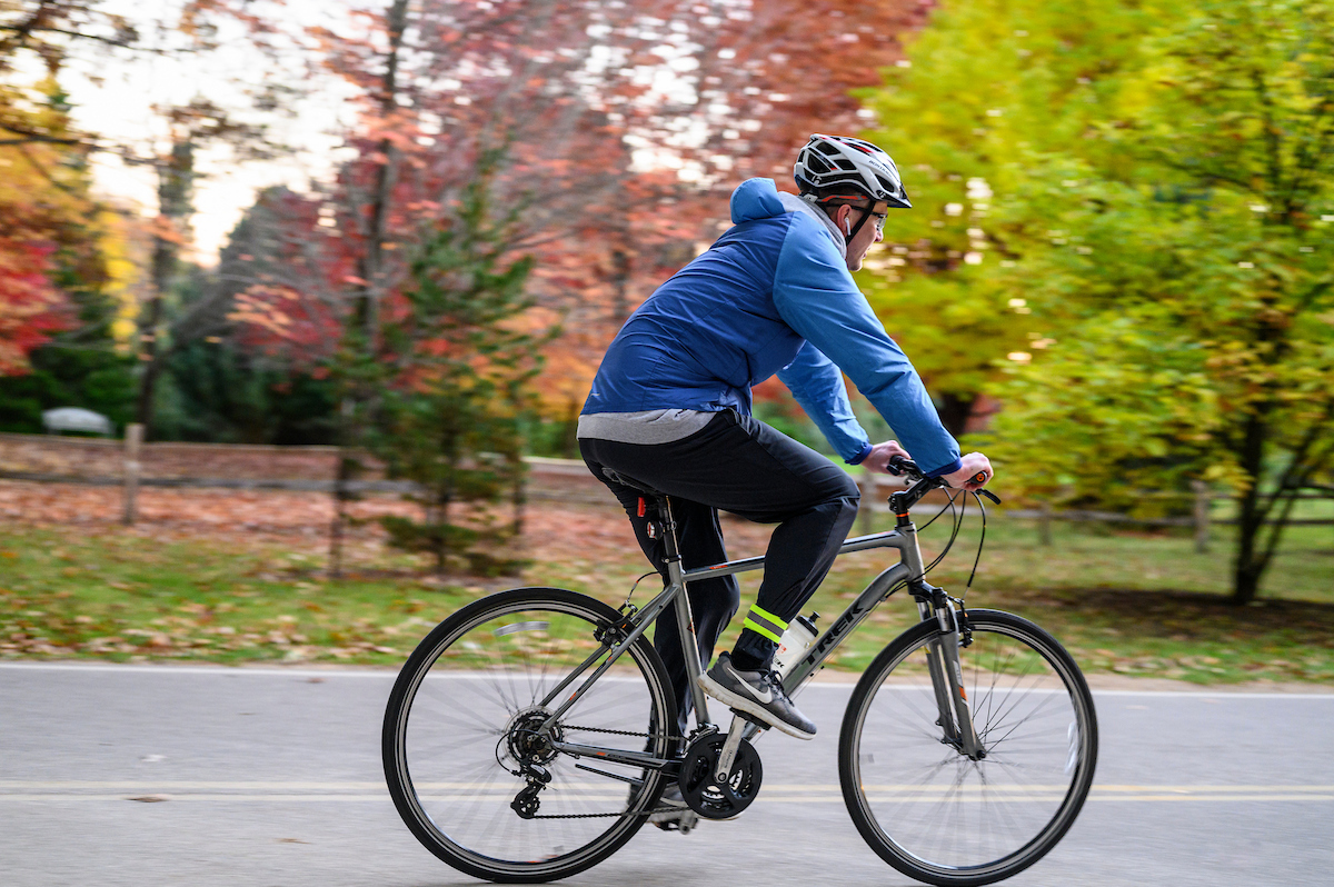 A bicyclist rides their bike along Arboretum Drive at University of Wisconsin–Madison Arboretum, past a forest of trees and foliage.