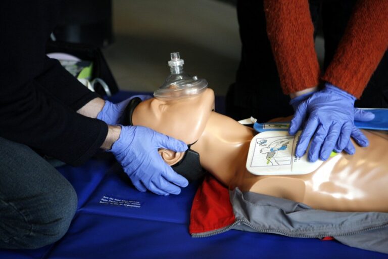 Two people perform CPR on a test dummy.
